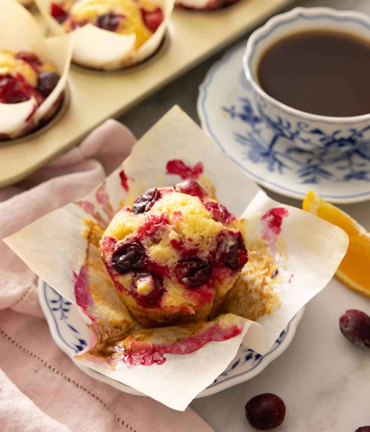 A plate with a cranberry orange muffins with the liner pulled open.