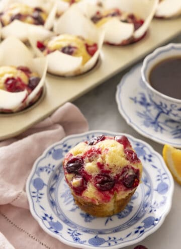 A plate with a cranberry orange muffin with more in the back.