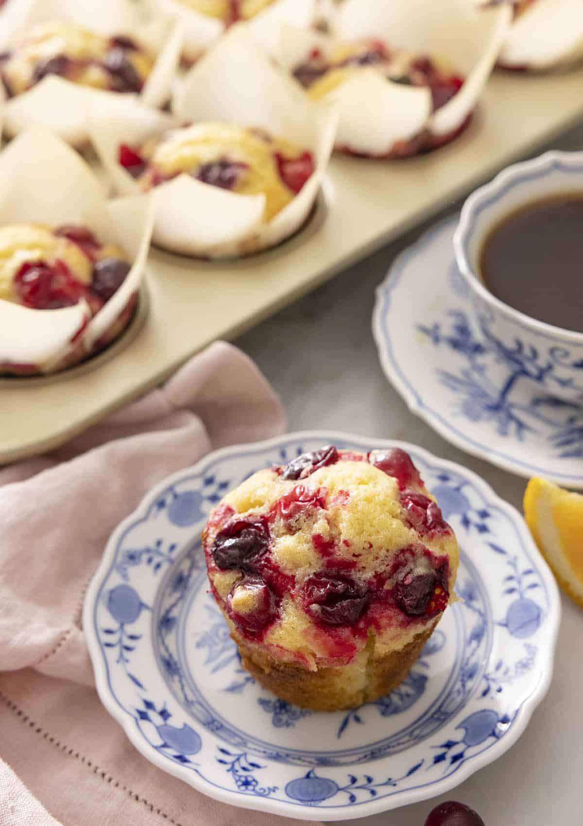 A plate with a cranberry orange muffin with more in the back.