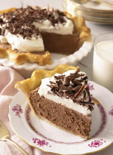 A slice of French silk pie on a plate in front of the rest of the pie.