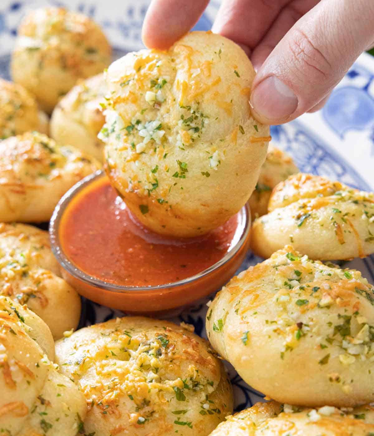 A garlic knot being dipped into sauce beside more knots.