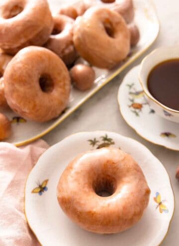 A plate with a glazed donut with a platter with more behind it.