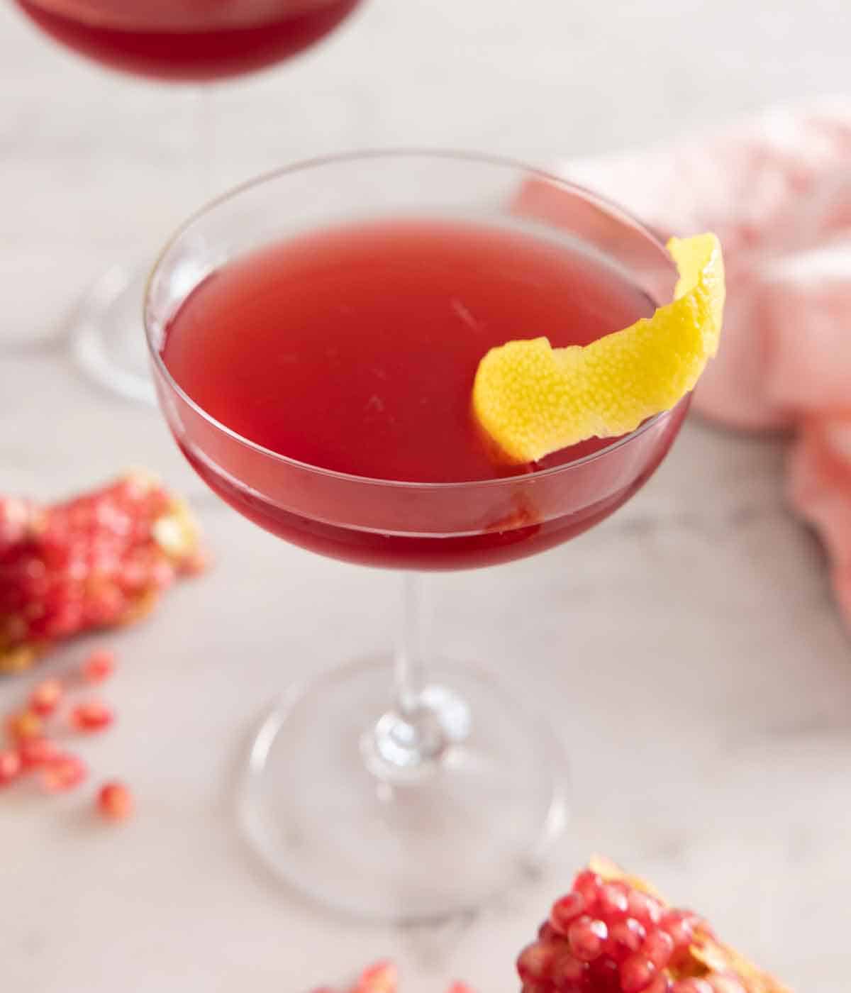 Close up of a glass of pomegranate martini with a lemon peel garnish.