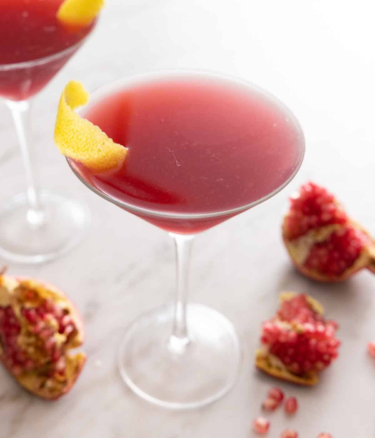 A glass of pomegranate martini with segments of fresh pomegranate scattered around.