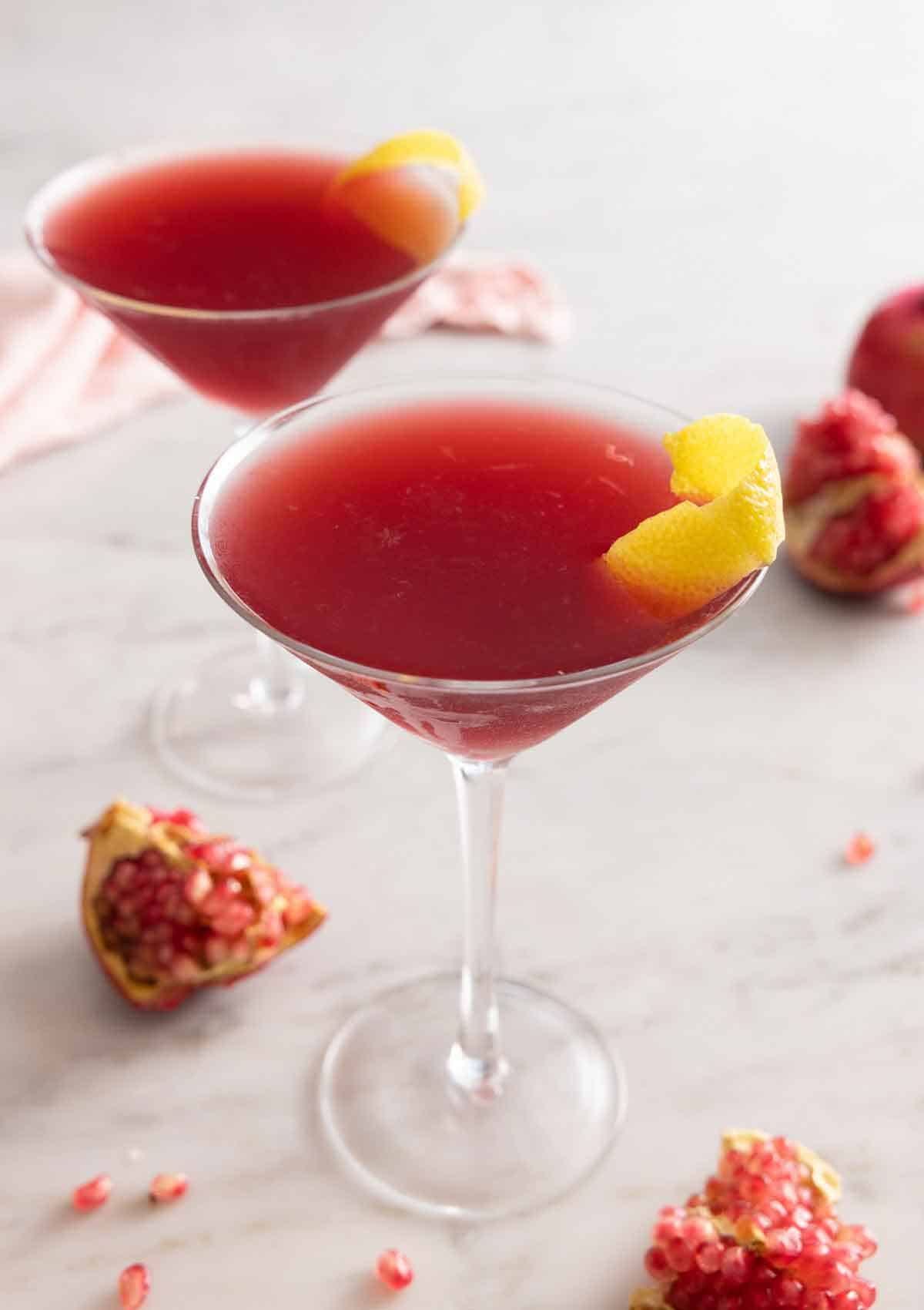 Two glasses of pomegranate martinis with lemon peel garnish.