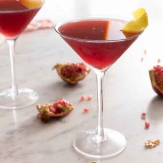 Two pomegranate martinis with fresh pomegranate segments on the counter.