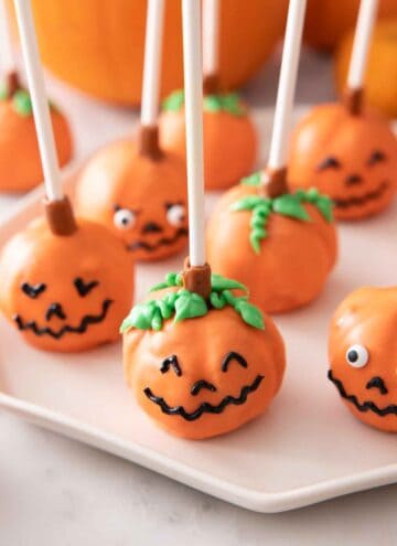 Multiple pumpkin cake pops with faces on a plate.