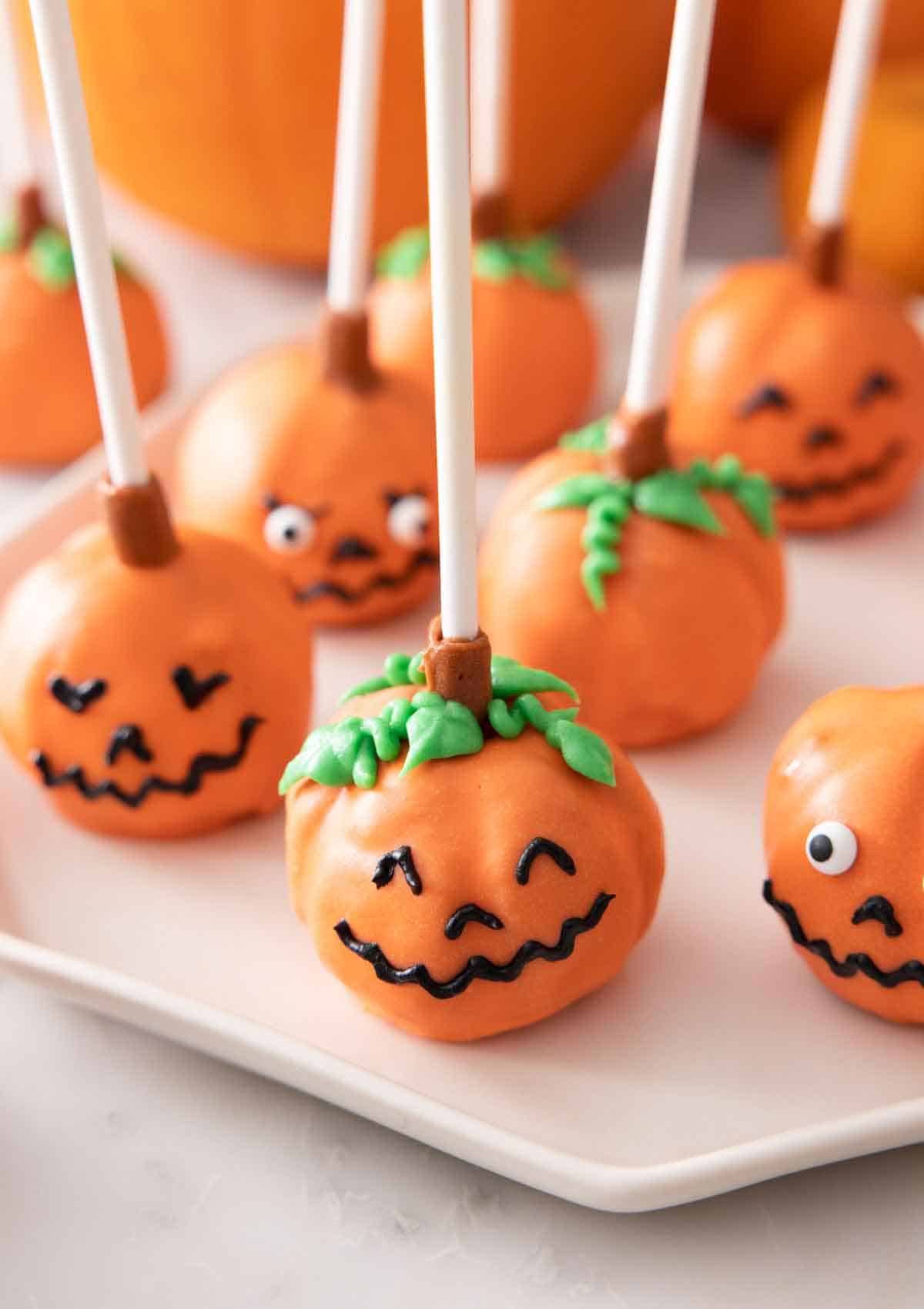 Multiple pumpkin cake pops with faces on a plate.