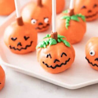 A plate with multiple pumpkin cake pops and one off to the side.