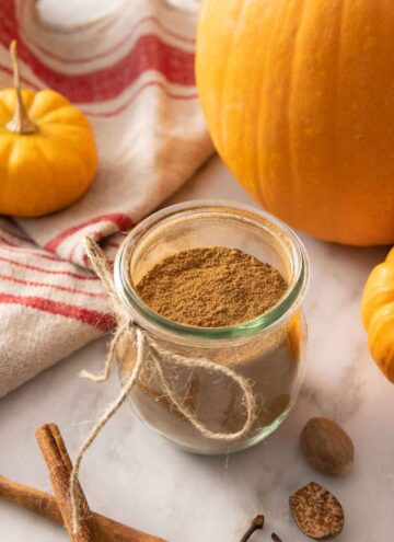 A tulip jar with pumpkin pie spice beside decorative pumpkins and scattered spices.