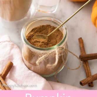 Pinterest graphic of a jar of pumpkin pie spice in a jar with a spoon inside of it. A latte with pumpkin pie spice sprinkled on top in the background along with a pumpkin.