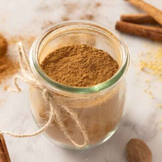 A tulip jar with pumpkin pie spice with cinnamon sticks and more spices scattered around the counter.