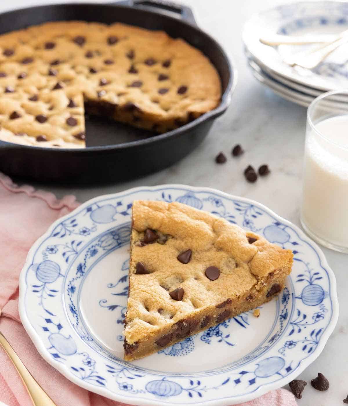 A plate with a slice of skillet cookie in front of the cast iron pan.