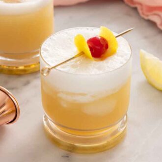 A glass of whiskey sour with a lemon wedge and jigger beside it.