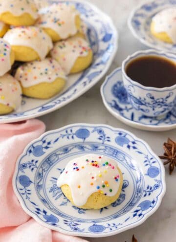 A plate with a anise cookie with sprinkles in front of a coffee.