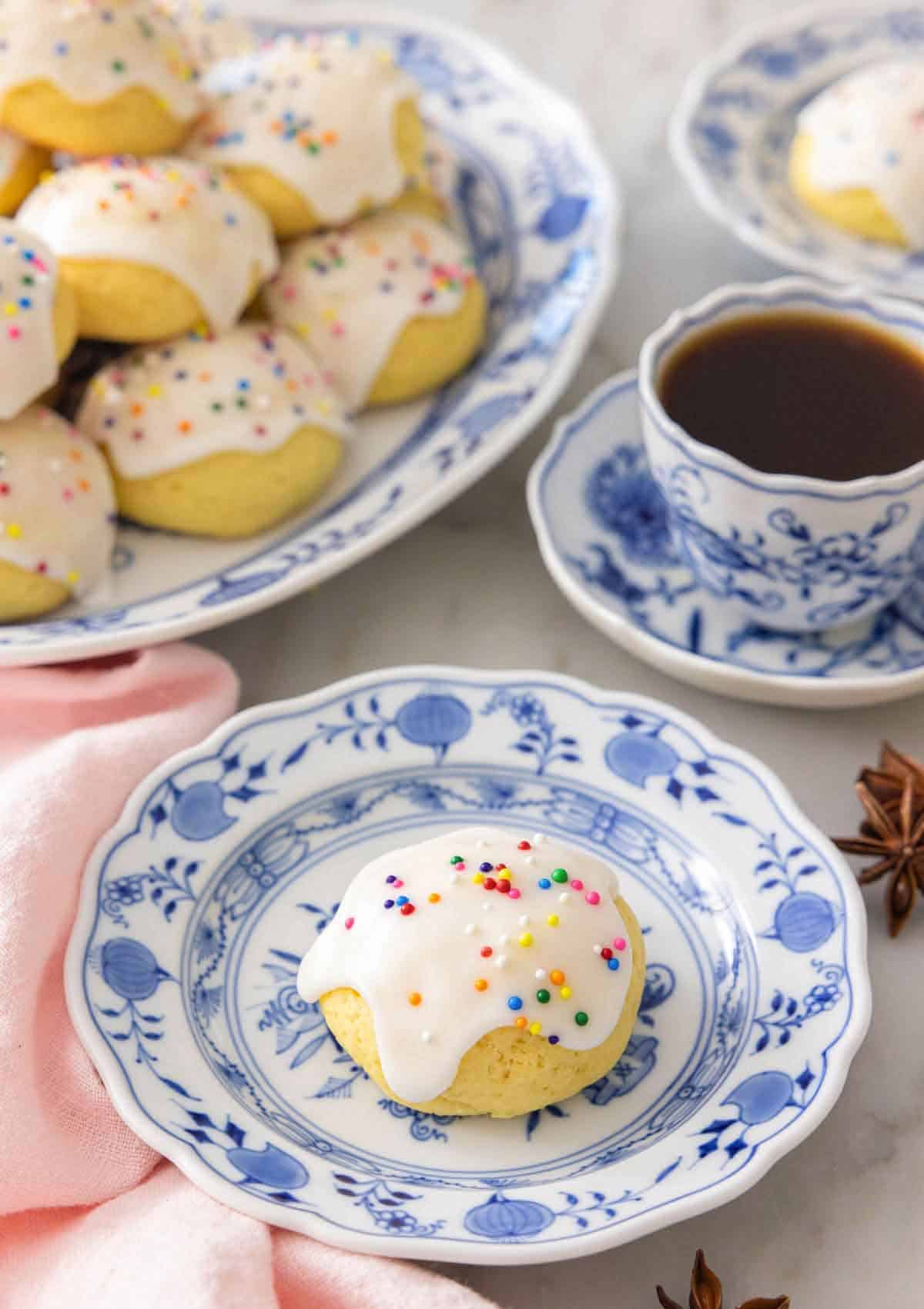 A plate with a anise cookie with sprinkles in front of a coffee.