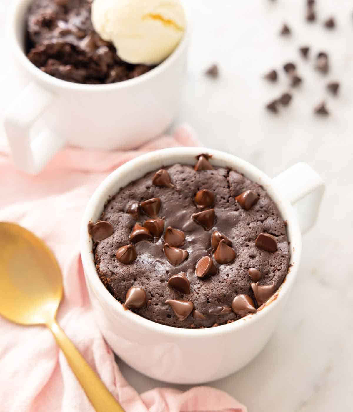 Overhead view of a brownie in a mug with a spoon beside it.