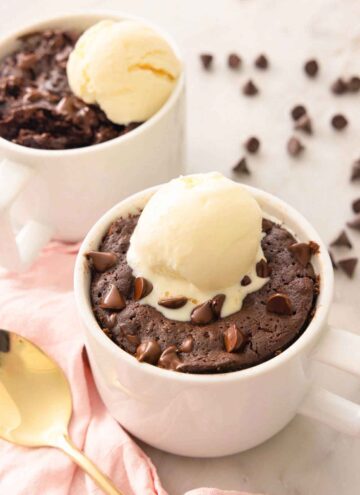 Two servings of brownie in a mug with a scoop of ice cream on top.