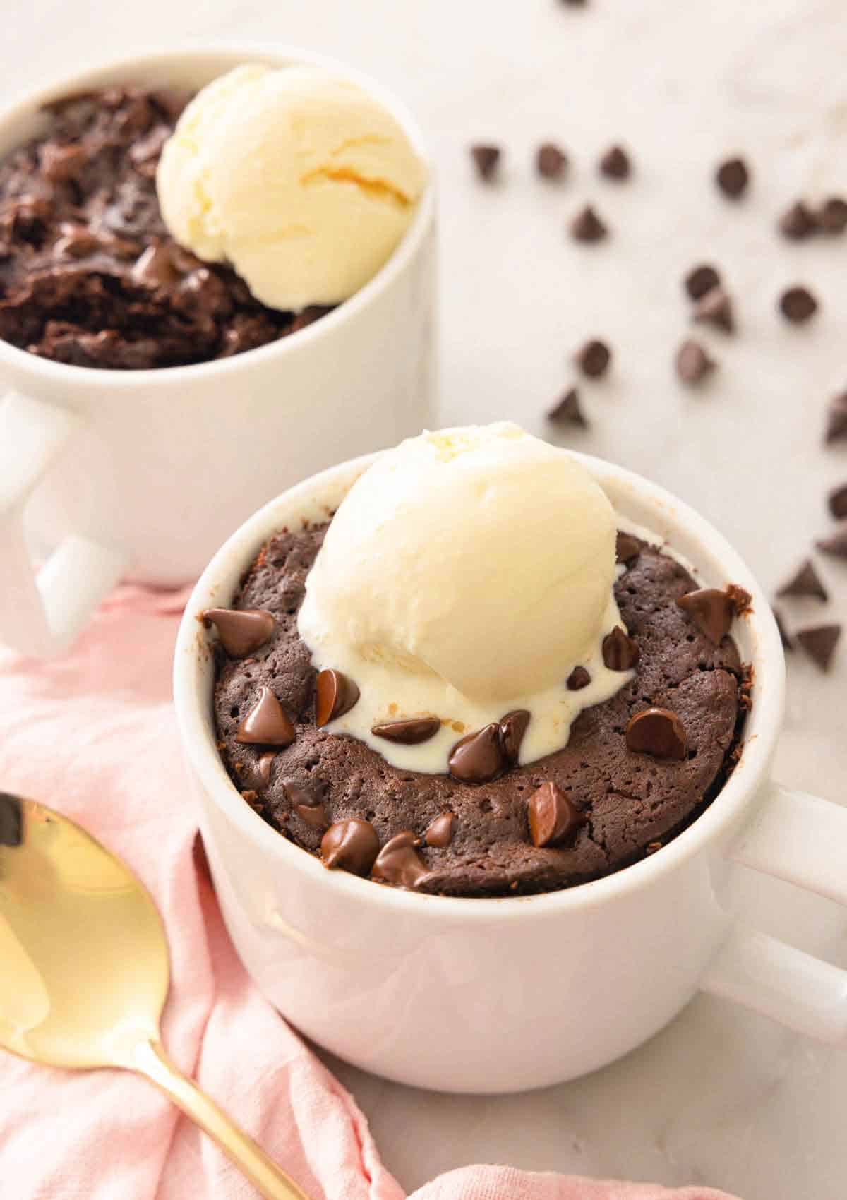 Two servings of brownie in a mug with a scoop of ice cream on top.