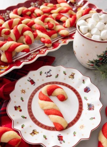A plate with a candy cane cookie in front of a platter of them.