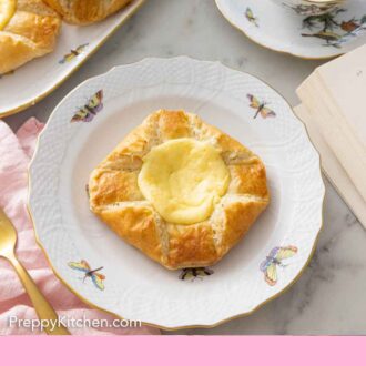 A plate with a cheese danish in front of a cup of tea.