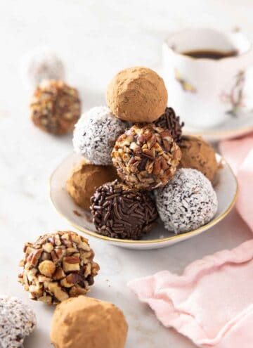 A plate with a pile of chocolate truffles with different coatings. A few in front.