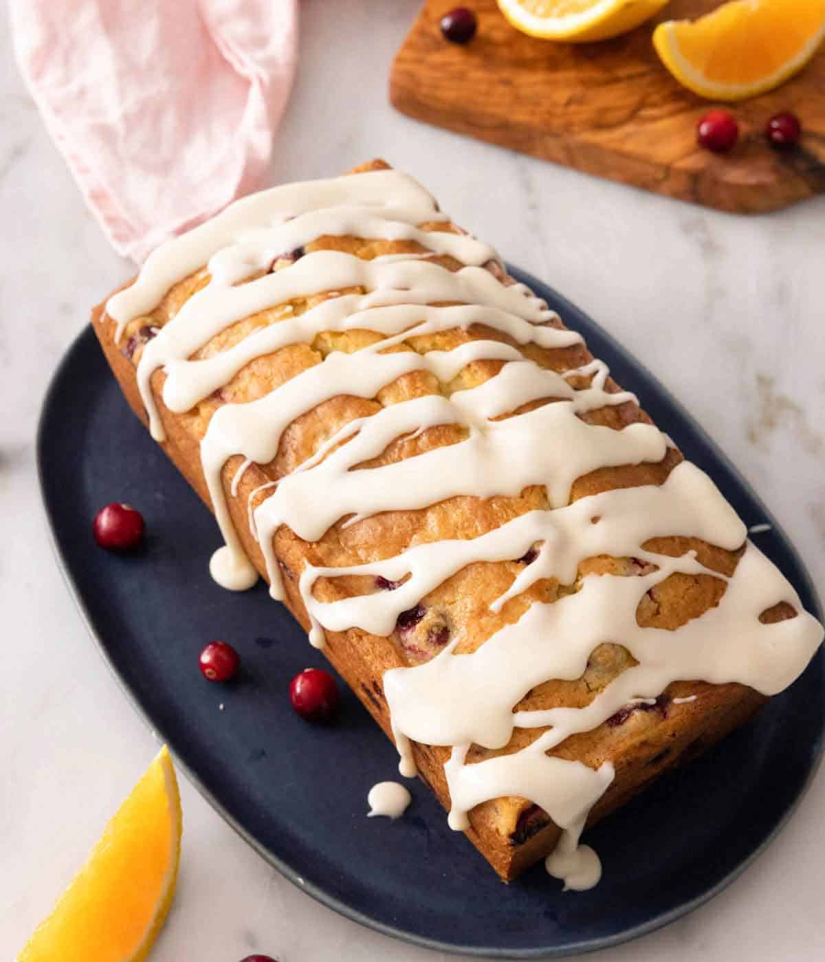 A platter with a loaf of cranberry orange bread with glaze drizzled on top.