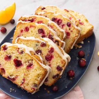 A serving platter of sliced cranberry orange bread with orange and cranberries around it.