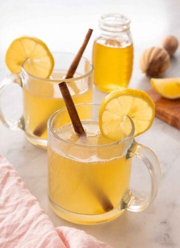 A glass of hot toddy in front of a second on and a jar of honey.