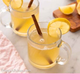 Pinterest graphic of hot toddy in two glasses with lemon and cinnamon.