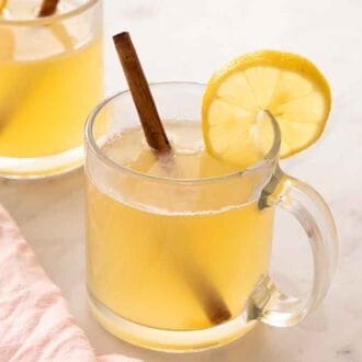 Two glasses containing hot toddy with a lemon slice and cinnamon stick as garnish.