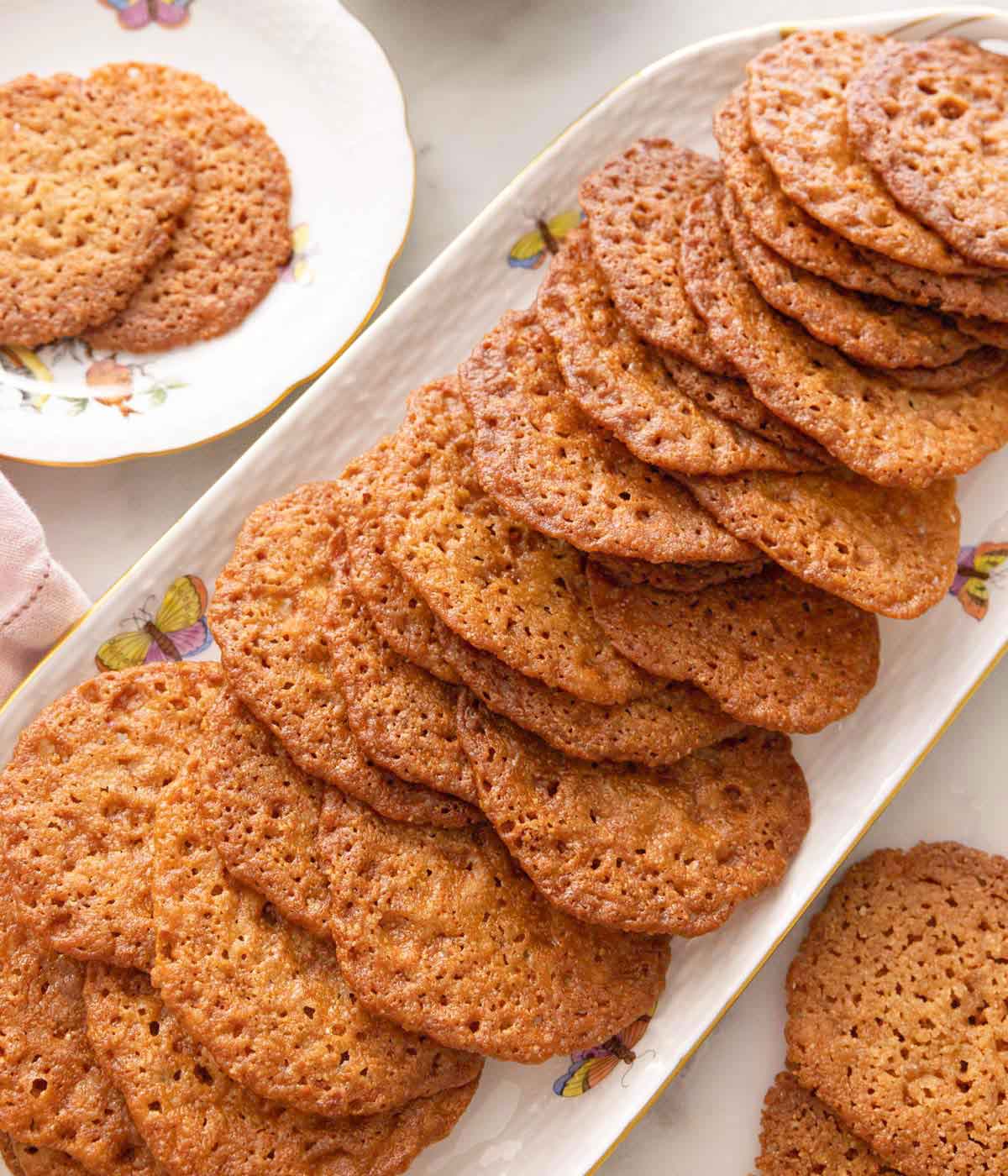 A platter filled with lace cookies with more around it.