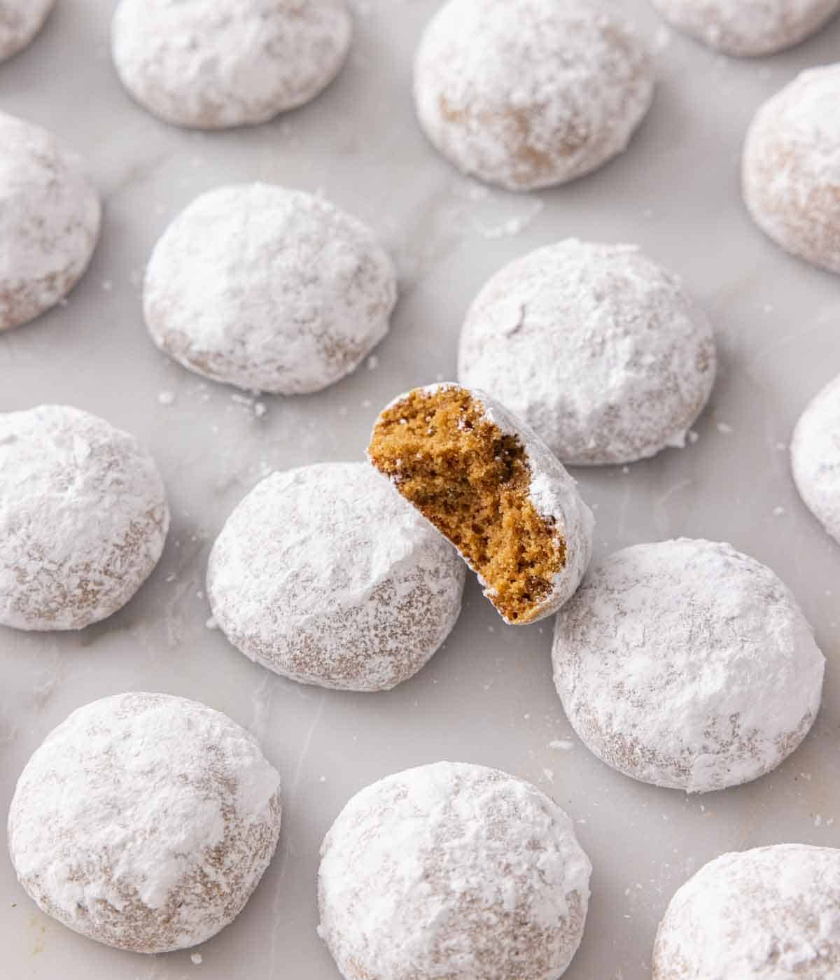 Multiple Pfeffernusse cookies in a single layer on a flat surface with one with a bite taken out, propped on top.