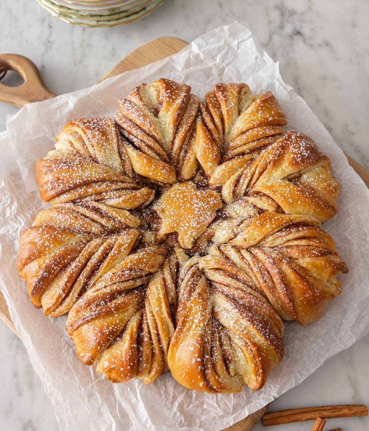 A star bread on top of parchment paper with powdered sugar dusted on top.