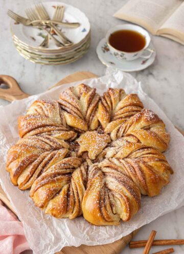 A star bread with powdered sugar dusted on top beside a cup of tea.