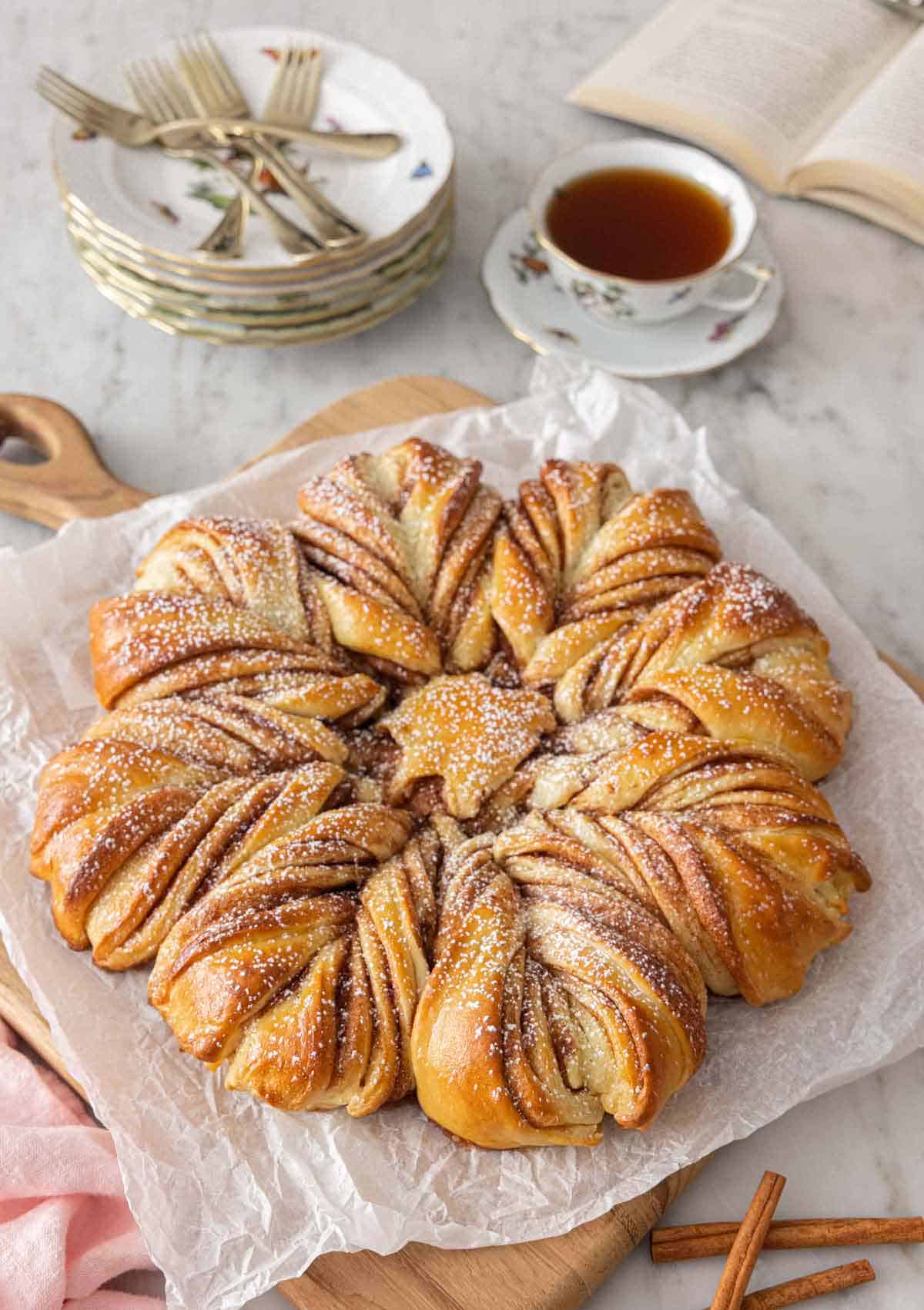 A star bread with powdered sugar dusted on top beside a cup of tea.