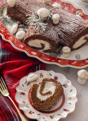 A Yule log on a platter with a slice of the cake on a plate in front of it.