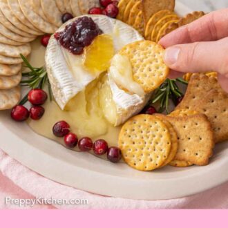 Pinterest graphic of a cracker scooping out baked brie from the cheese platter.