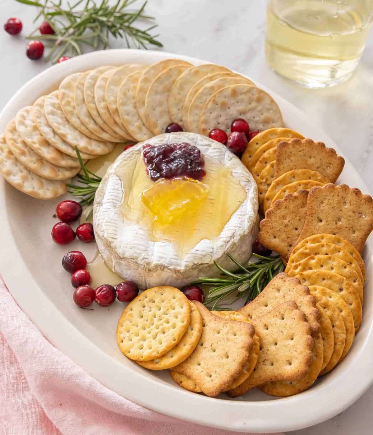 A platter of baked brie with crackers around it and honey, jam, and cranberries on top.