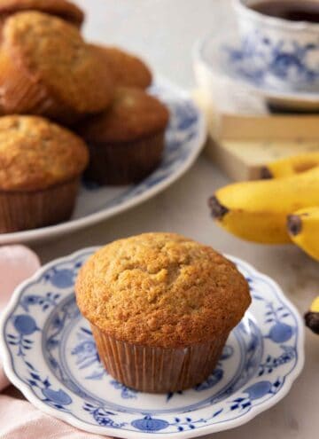 A plate with a banana muffin with a platter in the back.