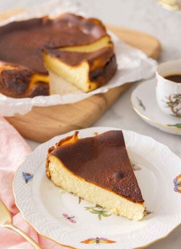 A slice of basque cheesecake on a plate in front the rest of the cake.