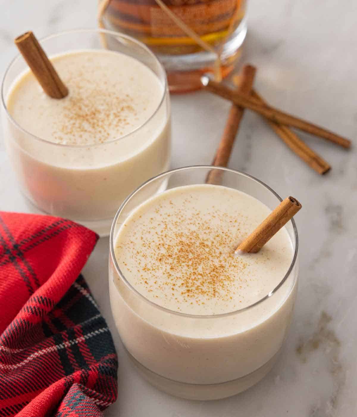 Glasses of coquito with cinnamon dusted on top and cinnamon sticks inside.