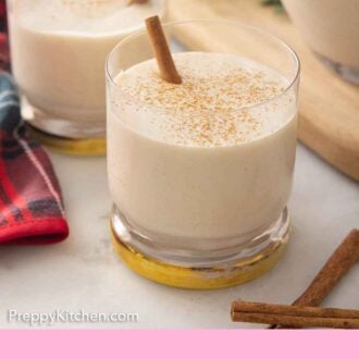 Pinterest graphic of two glasses of coquito with cinnamon dusted on top.