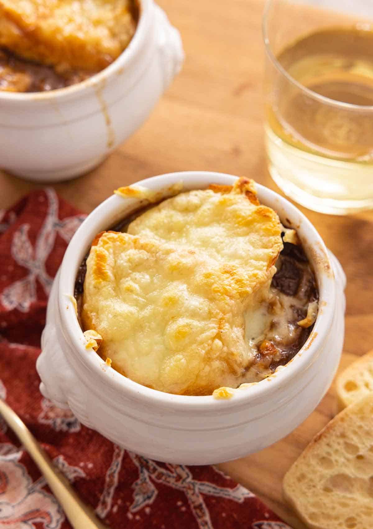 A serving of French onion soup with a glass of wine in the back.