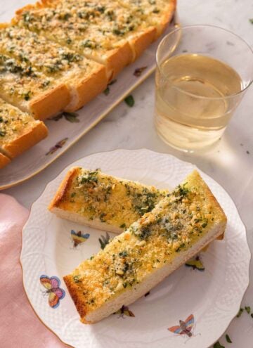 A plate with two pieces of garlic bread by a glass of wine.