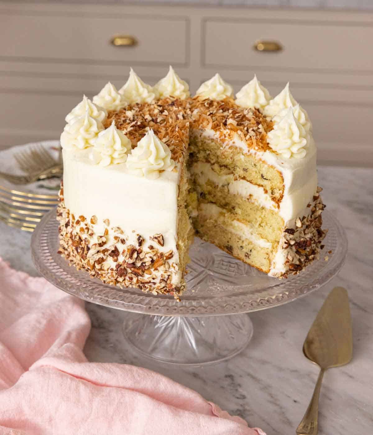 A cake stand with an Italian cream cake with a slice cut out.