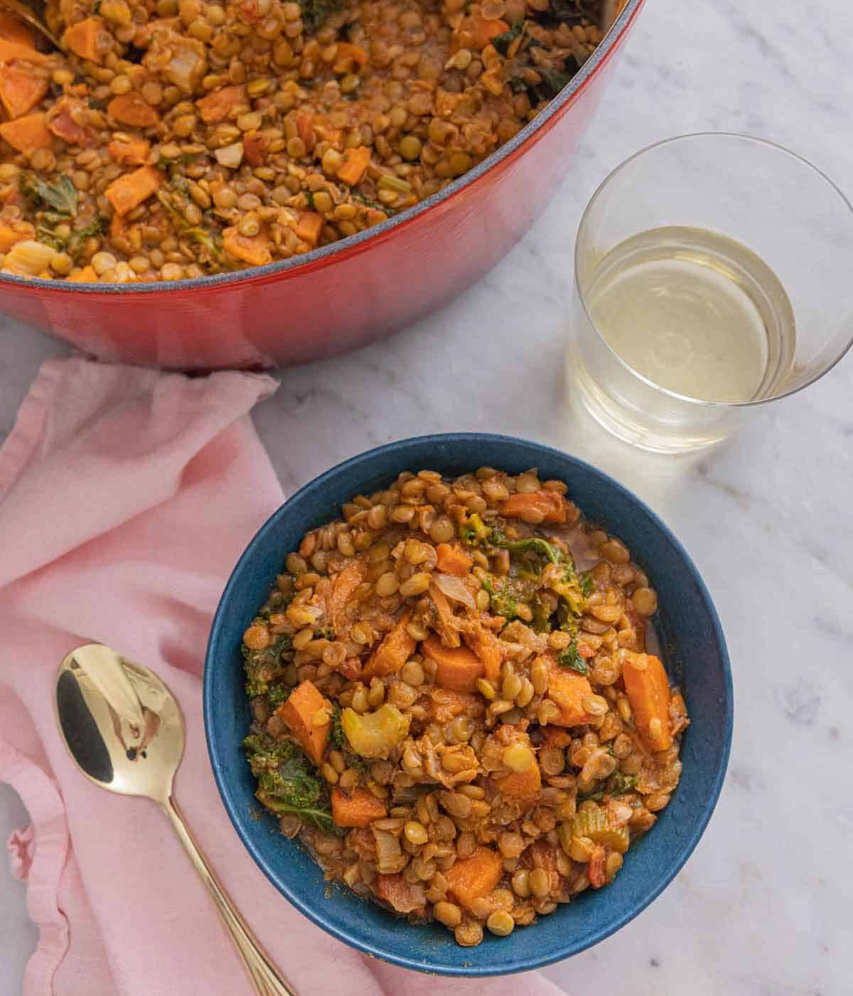Overhead view of a bowl of lentil soup by a glass of wine and a pot of more soup.