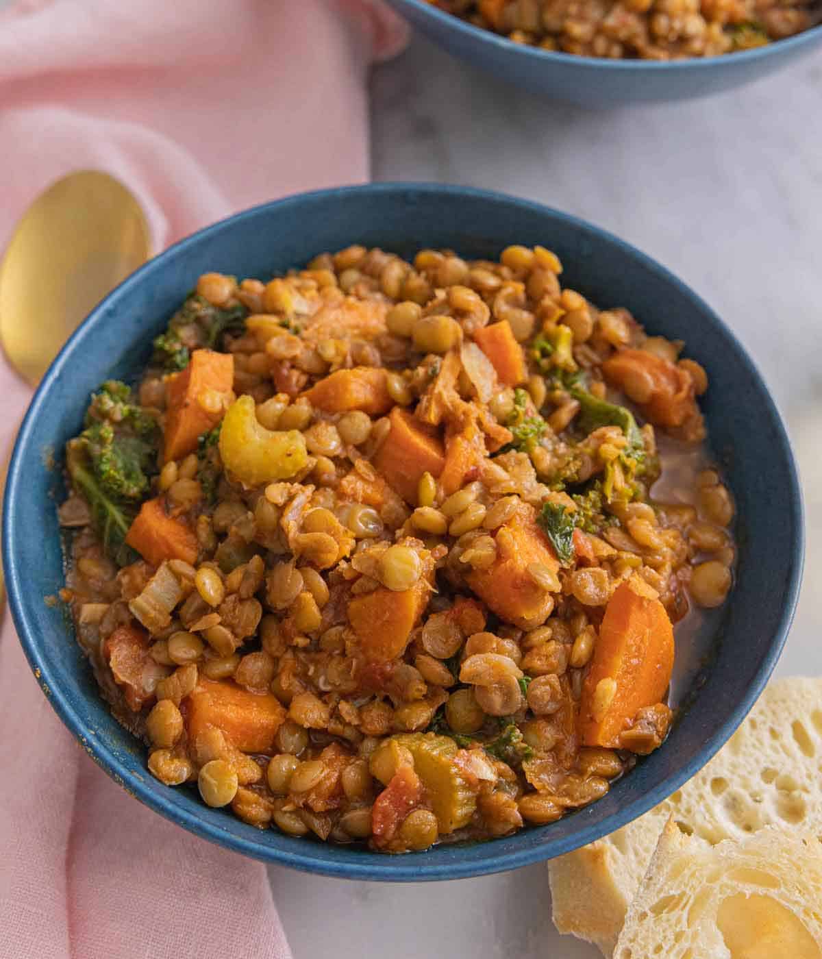 A blue bowl with lentil soup by a pink linen napkin.