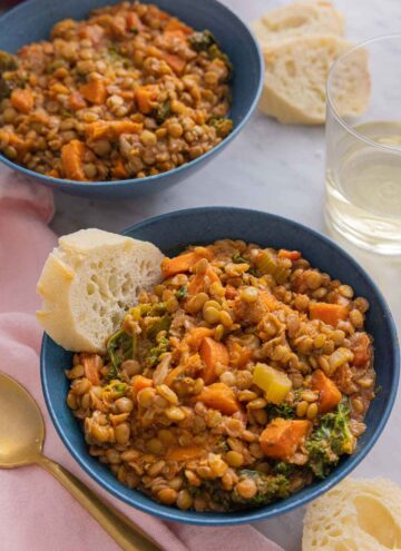Two bowls of lentil soup with one served with bread.