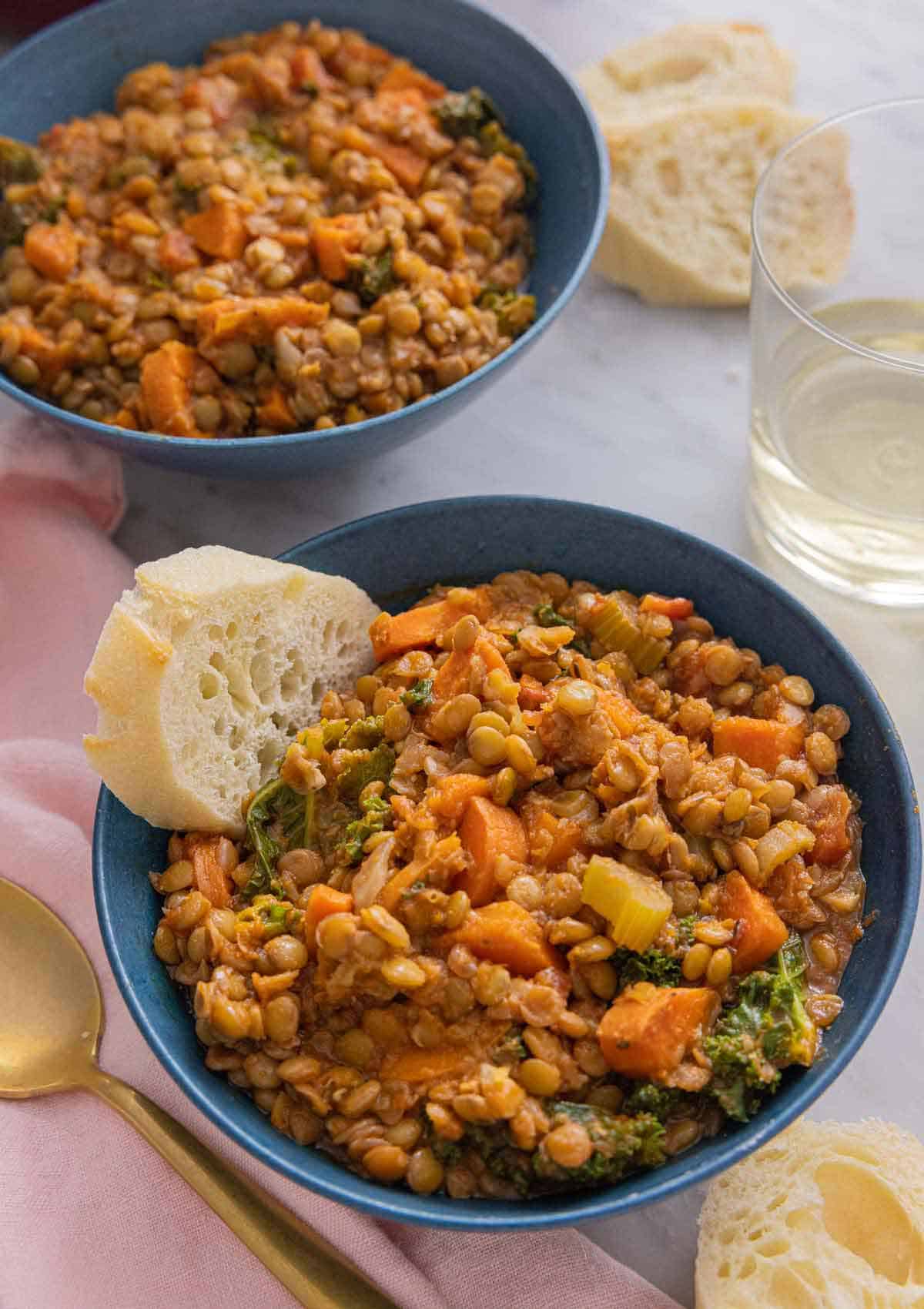 Two bowls of lentil soup with one served with bread.